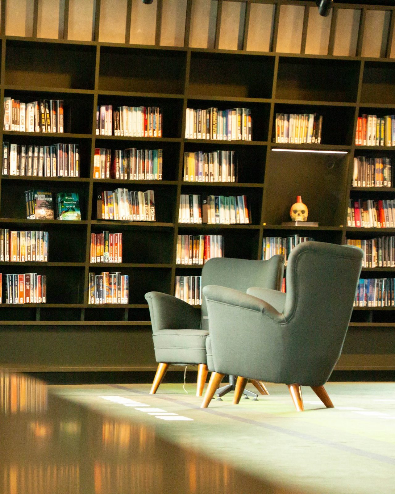 Foto: Leseecke mit zwei Sesseln vor hohen Bücherregalen in einer Bibliothek.