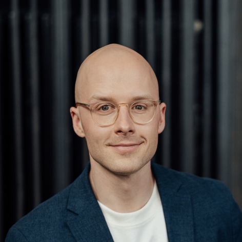 Portrait photo of the lecturer, Dr. Tobias Vlćek, smiling, with glasses and a dark blazer.